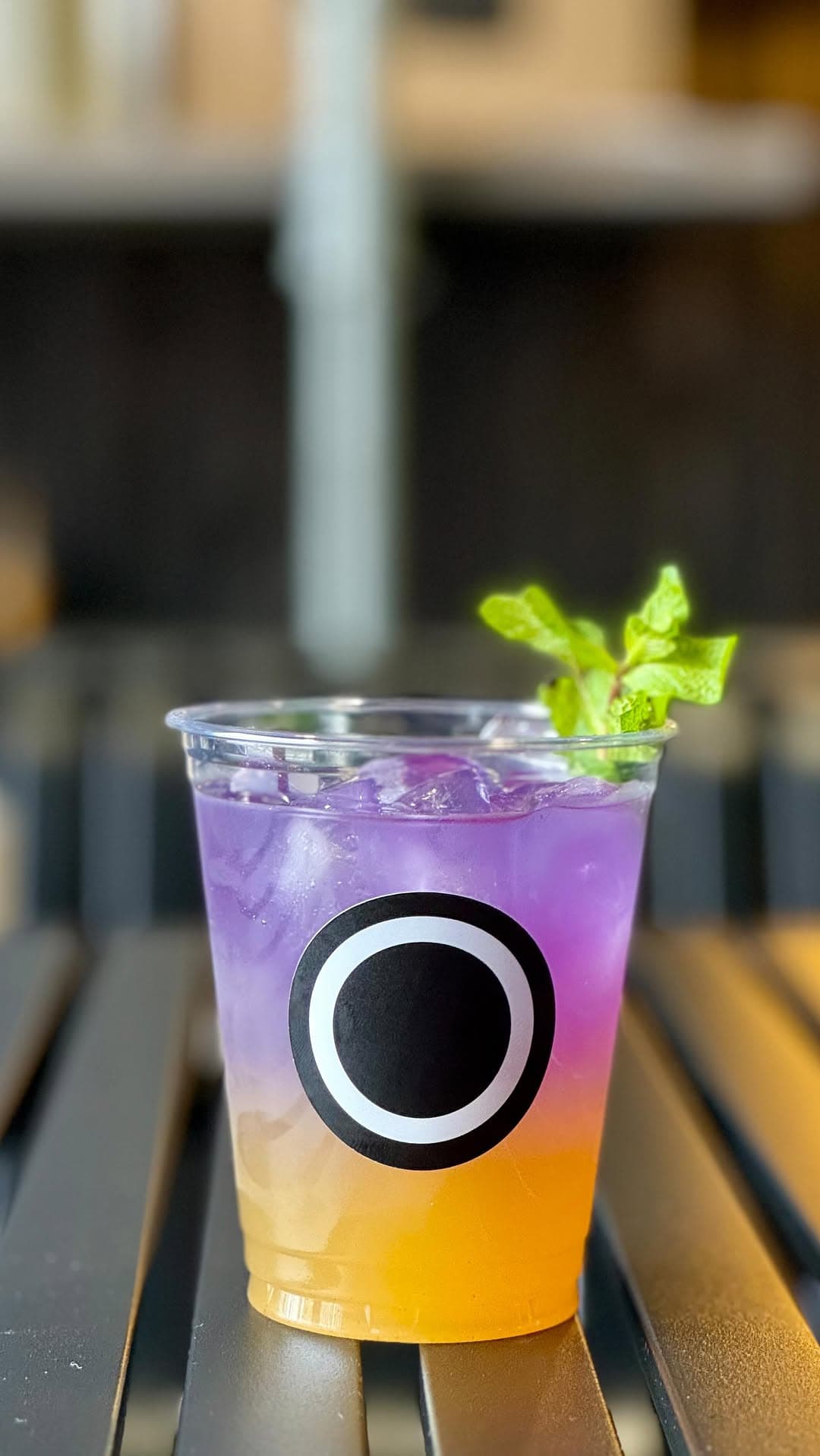 Purple-to-amber gradient lemonade in a clear cup, the concentric Hollow Oak O mark printed dead centre.