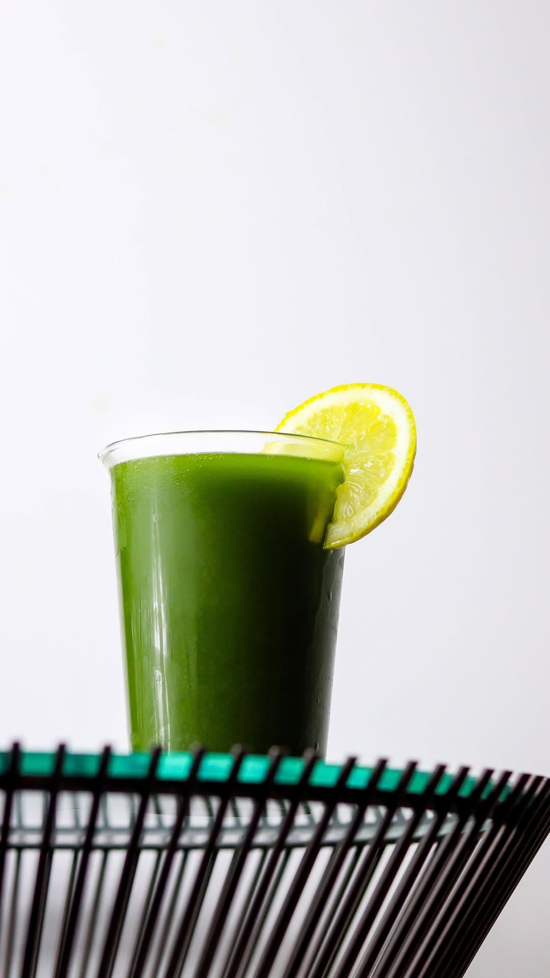 Bright green cold-pressed juice with a wedge of lemon.